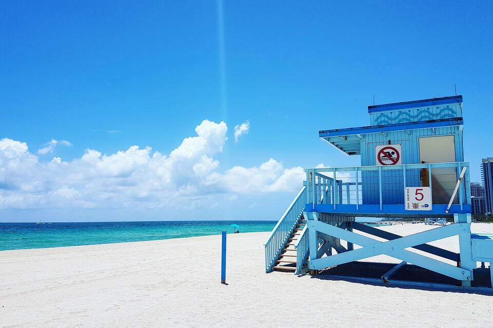 Una torre de salvavidas en una playa arenosa, con cielo azul despejado y océano.