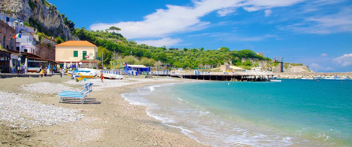 A beach with pebbles, a pier, boats, and buildings.