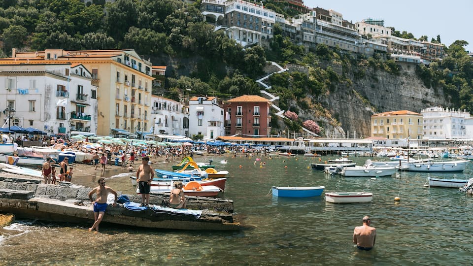 A crowded beach with boats and people.