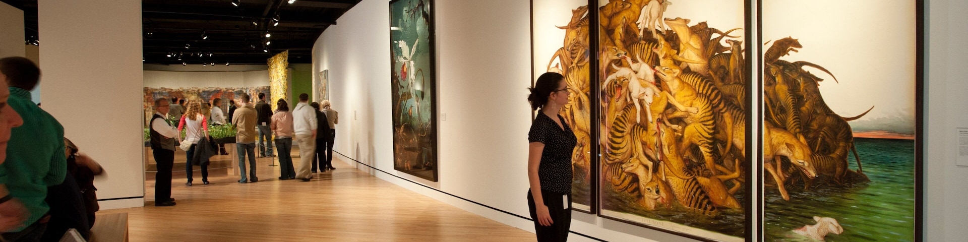 Une galerie d’art où de grandes peintures ornent les murs et où les visiteurs observent les œuvres.
