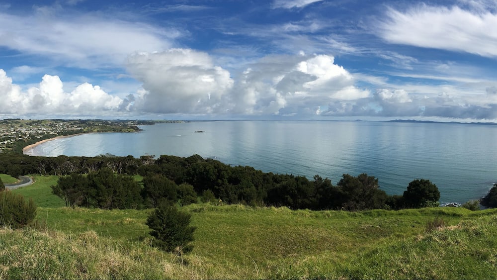 Un paysage côtier comprenant une plage, une ville et des collines ondulantes.