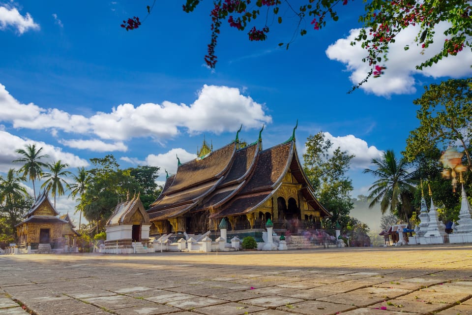 A traditional temple with tiered roofs, palm trees, and a clear blue sky.