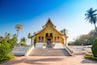 A temple with a golden roof and white walls, surrounded by palm trees and a clear blue sky.