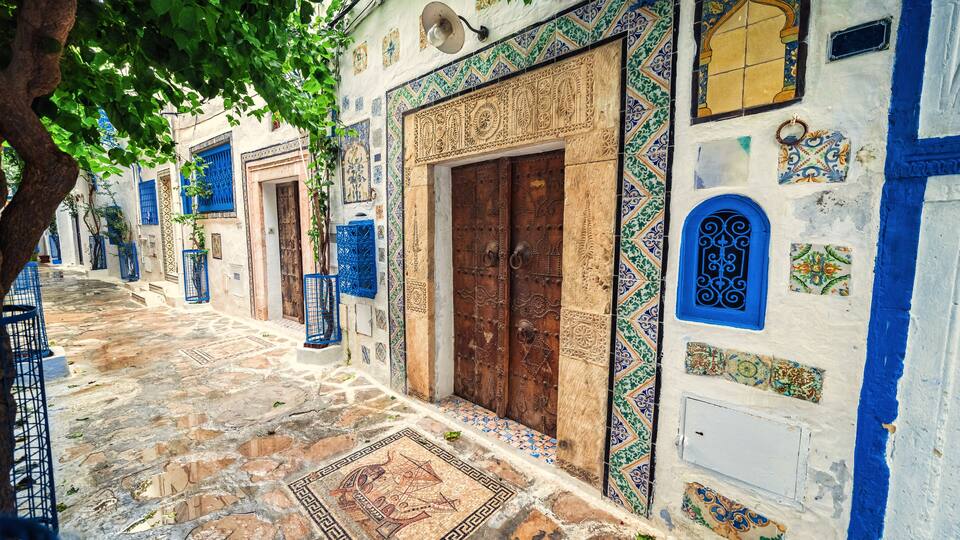 A narrow cobblestone street lined with buildings featuring blue doors and intricate tile work.