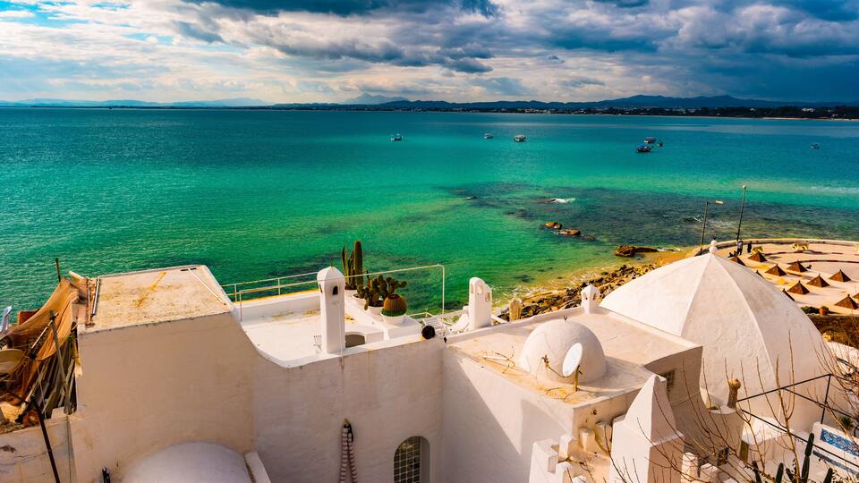 A coastal town with white buildings, a clear blue sea, and boats.