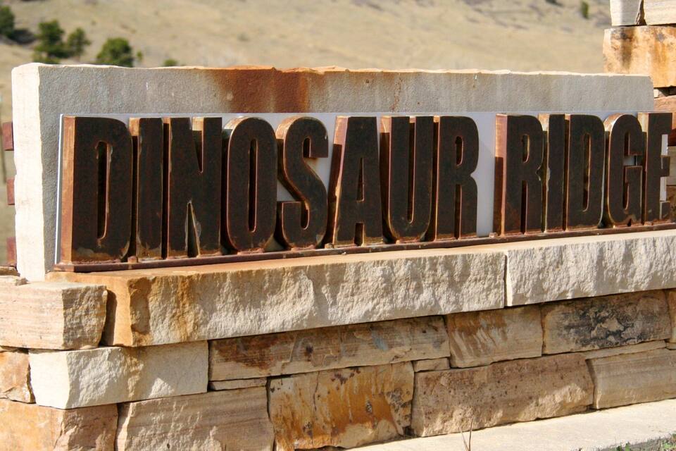 Segnaletica con la scritta 'DINOSAUR RIDGE' fissata a un muro di pietra.