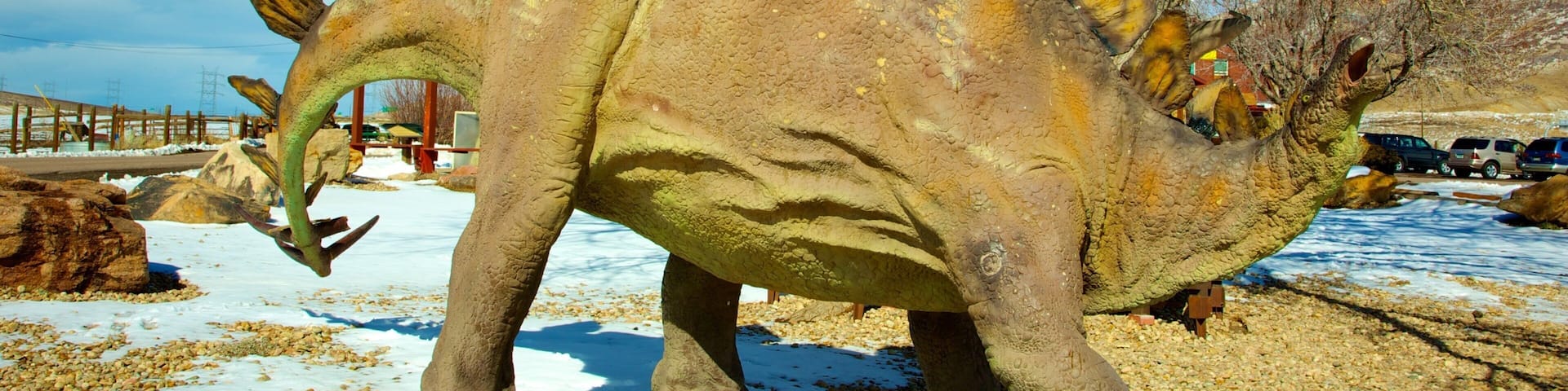 A dinosaur statue with a textured surface and leaf-like structures on its back, set against a backdrop of trees and a clear sky.
