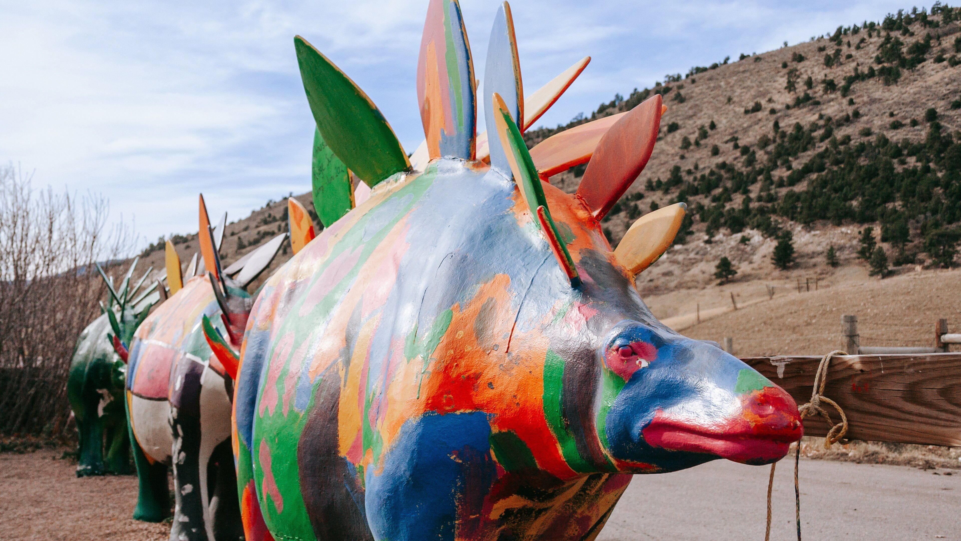 Una escultura pintada de colores que representa un pez con aletas puntiagudas, con un paisaje montañoso de fondo.