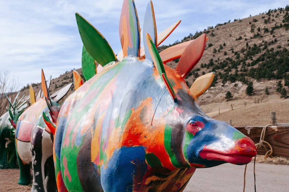 A colorful painted sculpture of a fish with spiky fins, set against a backdrop of a hilly landscape.