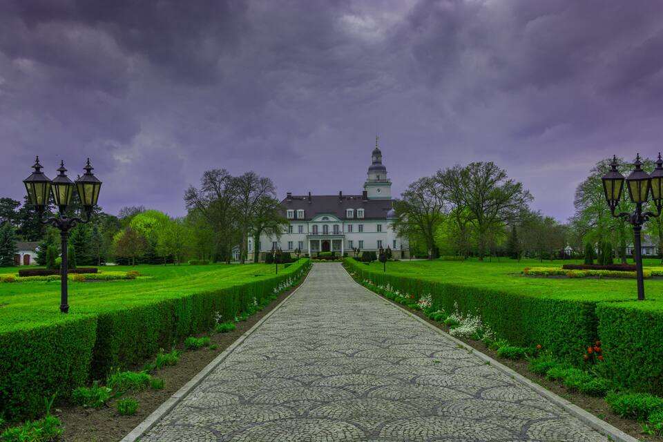A grand building with a symmetrical garden and a cobblestone pathway leading to it.