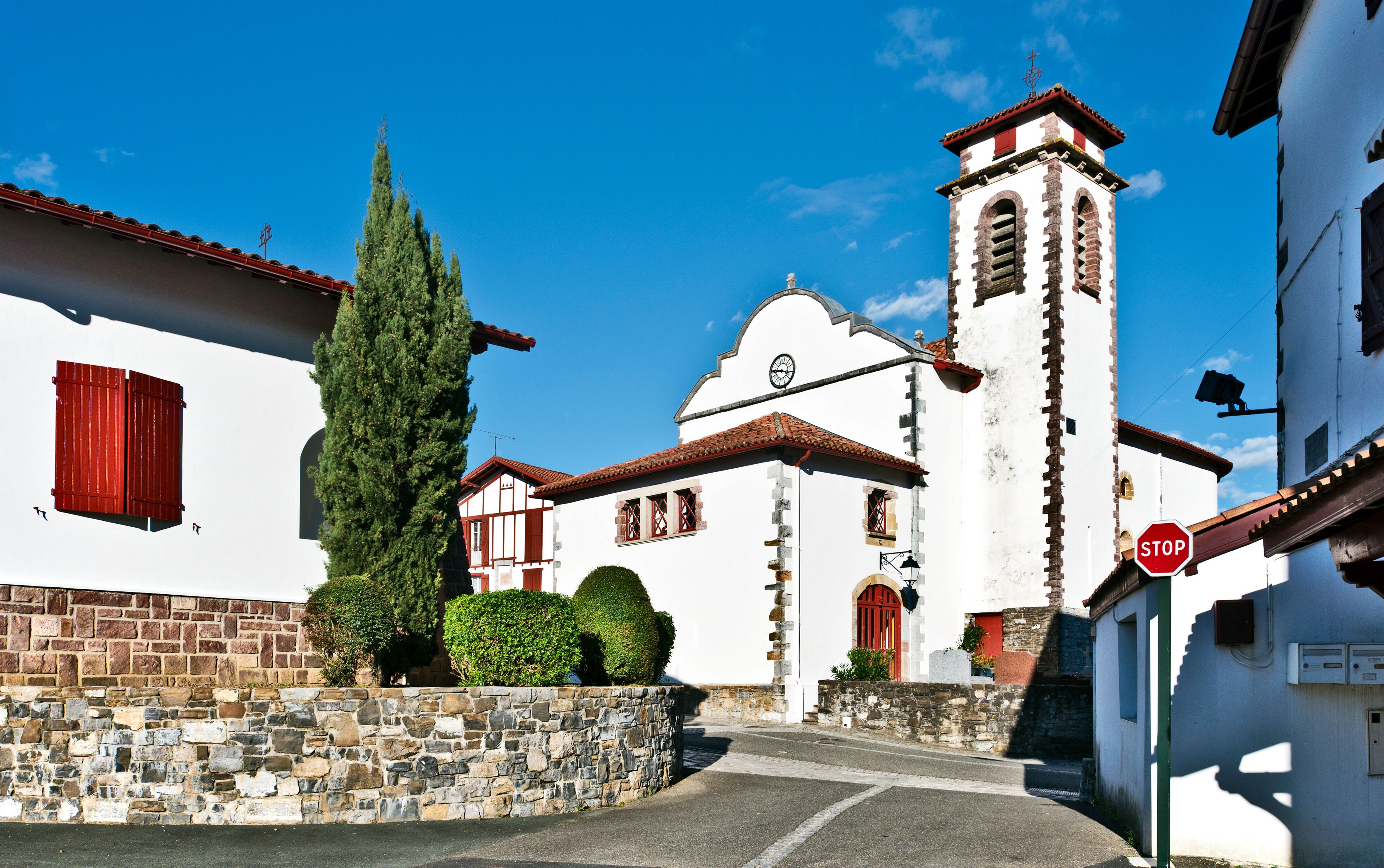 A white church with a clock tower, a stone wall, and a stop sign.