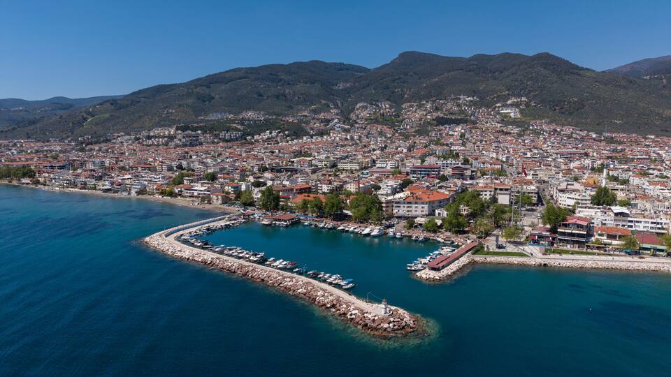 A coastal city with a marina, dense urban area, and mountains in the background.