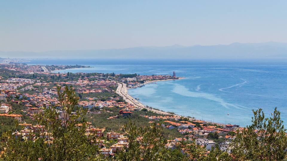 A coastal town with a beach, a bridge, and mountains in the background.