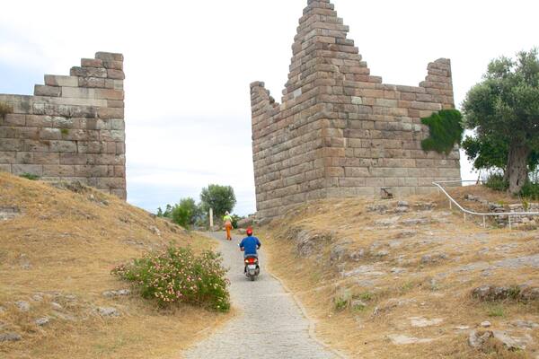 Un camino de piedra que lleva a unas ruinas antiguas, con una persona montando un patinete.