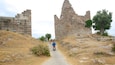 A stone pathway leading to ancient ruins with a person riding a scooter.