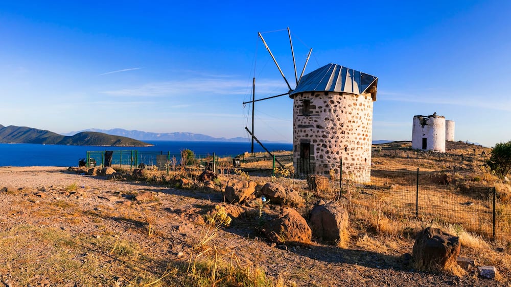 Un mulino a vento su una collina, con un cielo azzurro intenso e montagne sullo sfondo.