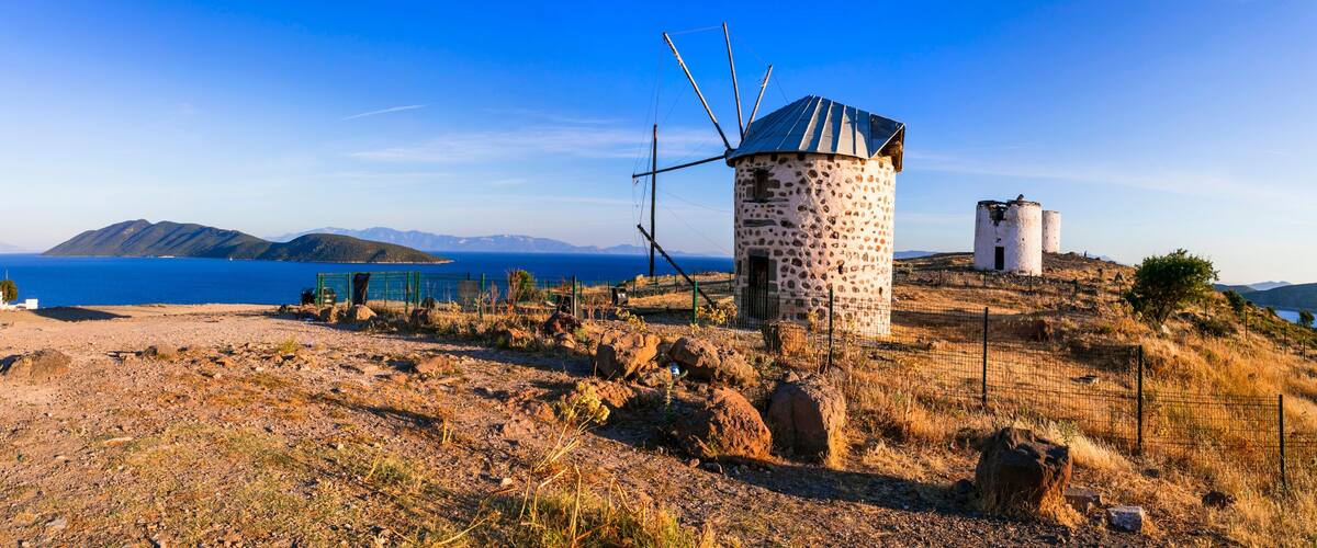 A windmill on a hillside with a clear blue sky and mountains in the background.