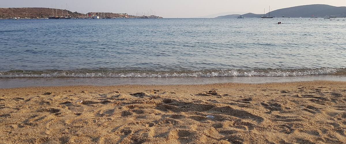 A beach with footprints in the sand and a calm sea with boats in the distance.