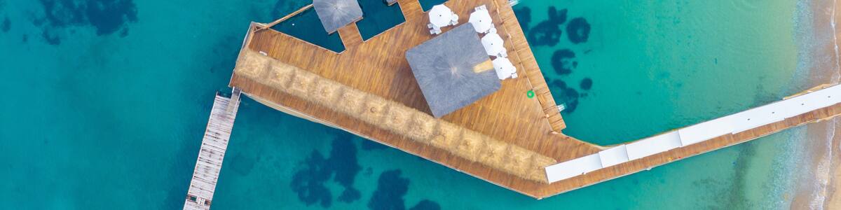 An aerial view of a resort with a wooden deck, lounge chairs, and a pier extending into turquoise waters.