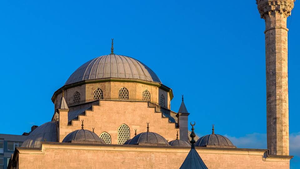 Eine Moschee mit einer großen Kuppel und einem hohen Minarett unter blauem Himmel.