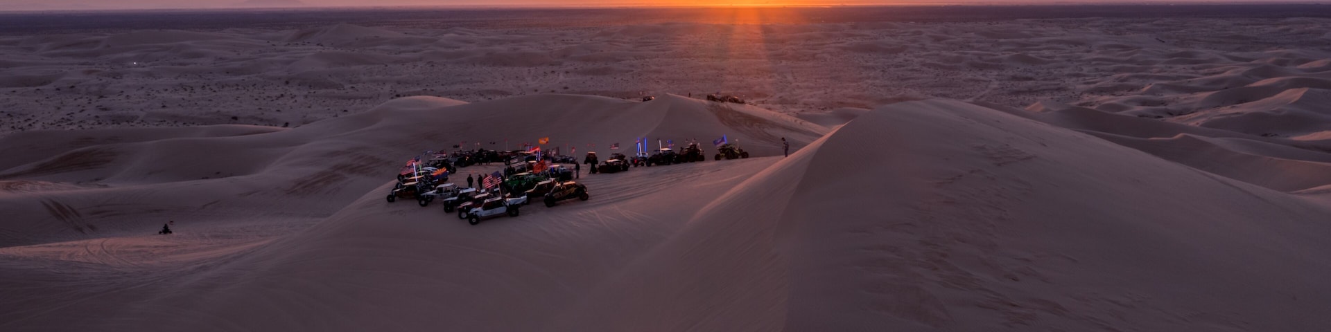 A desert landscape with sand dunes and a sunset in the background.