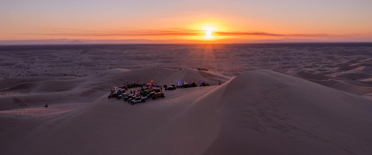A desert landscape with sand dunes and a sunset in the background.