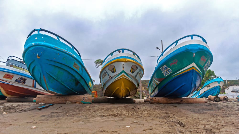 Low and wide angle view of several boats on the beach sand, on logs, on an overcast morning. Puerto Cayo, Manabi, Ecuador