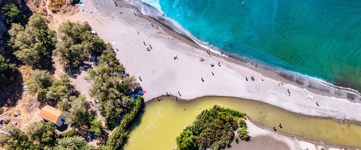 A coastal landscape with a sandy beach, clear turquoise waters, and a small river or lagoon.