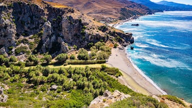 A coastal landscape with a rocky cliff, a beach, and a clear blue sea.