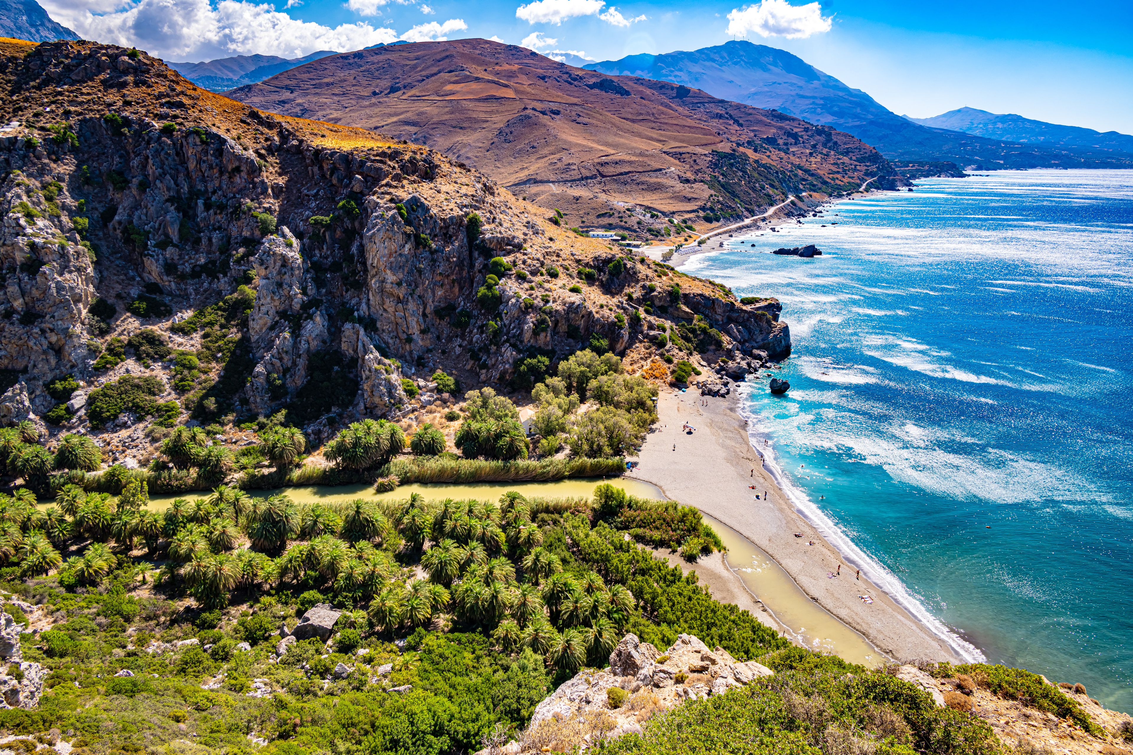 A coastal landscape with a rocky cliff, a beach, and a clear blue sea.
