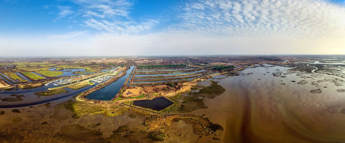 An aerial view of a coastal area with a river, farmland, and a large body of water.