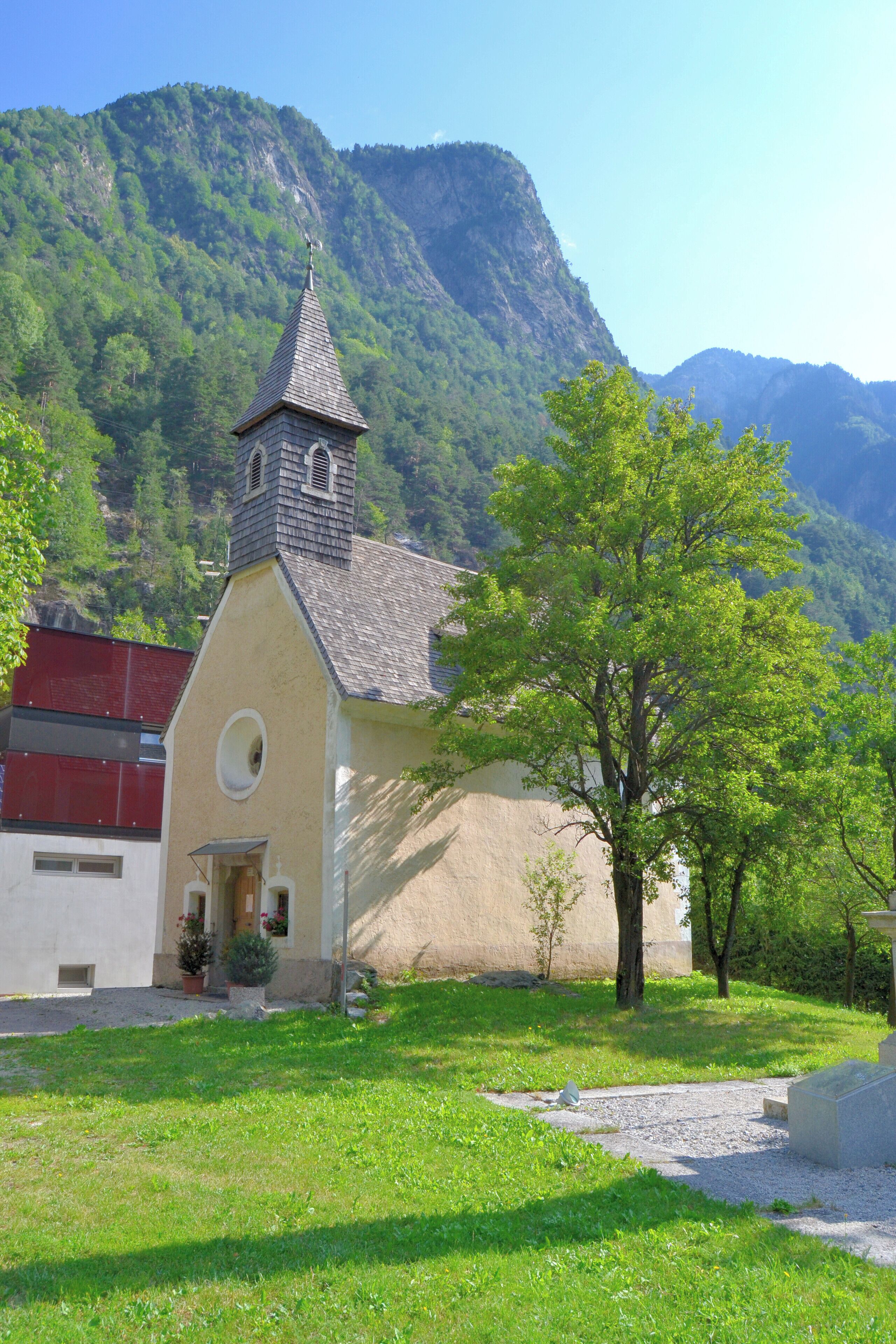 A church with a bell tower, surrounded by lush greenery and mountains in the background.