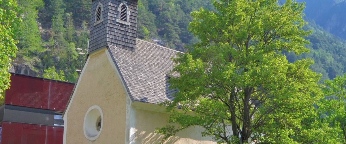 A church with a bell tower, surrounded by lush greenery and mountains in the background.