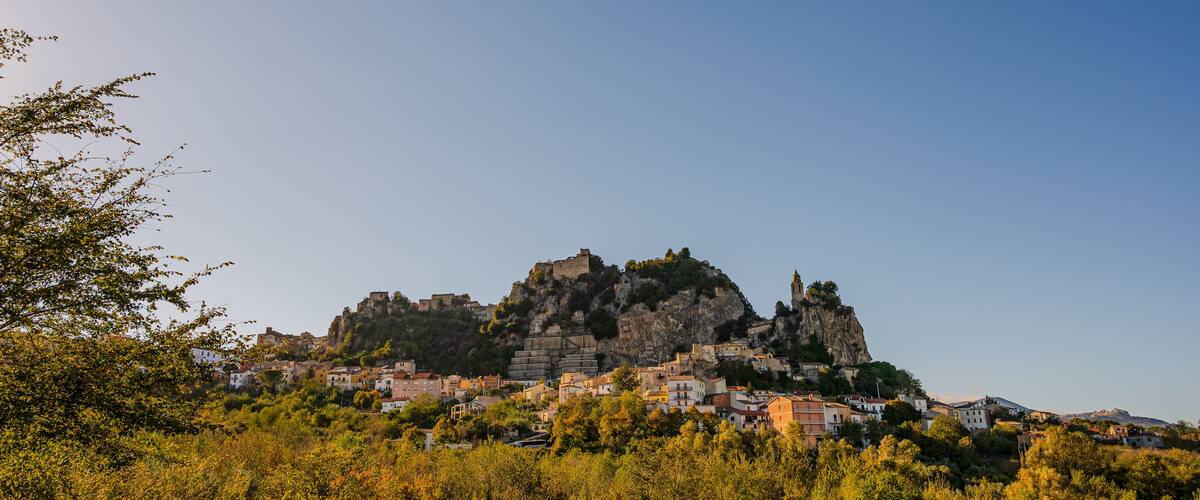 A historic town with a prominent castle on a hill, surrounded by lush greenery and traditional buildings.