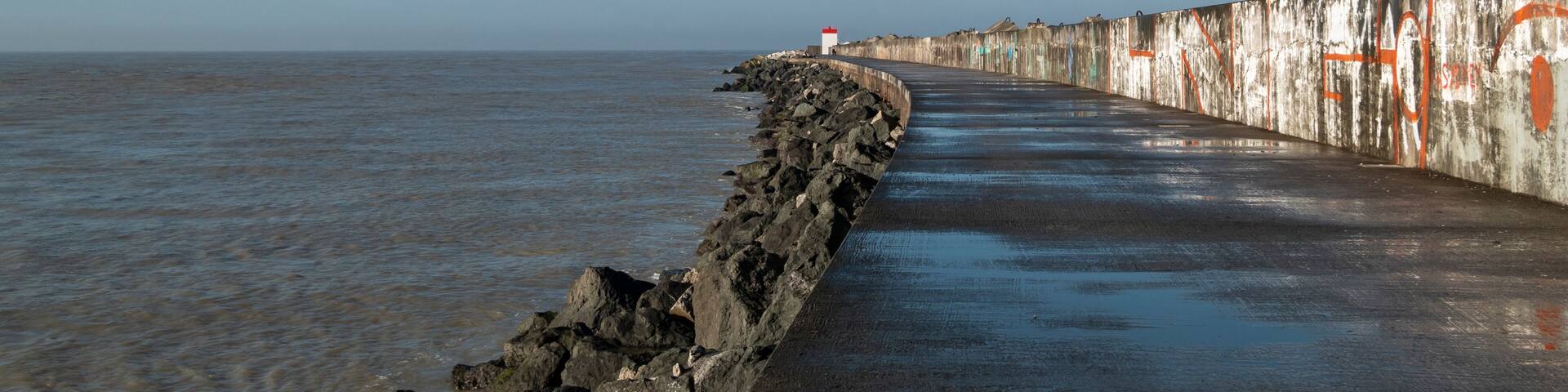 Dique na praia do Digue em Boucau com um farol ao fundo em França