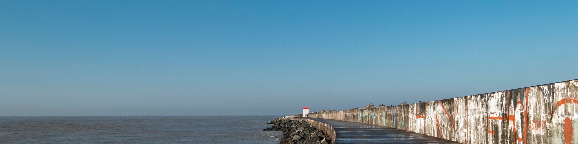 Dique na praia do Digue em Boucau com um farol ao fundo em França