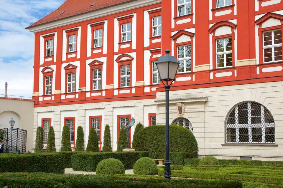 A red and white building with arched windows and a statue in the garden.