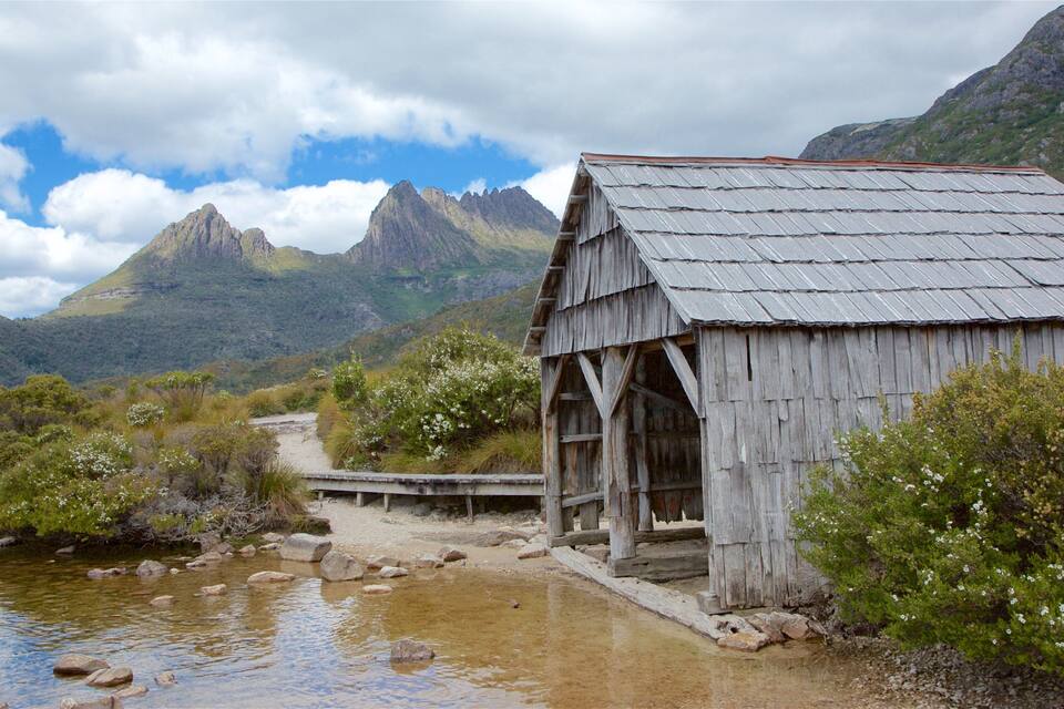 A wooden structure by a river with mountains in the background.