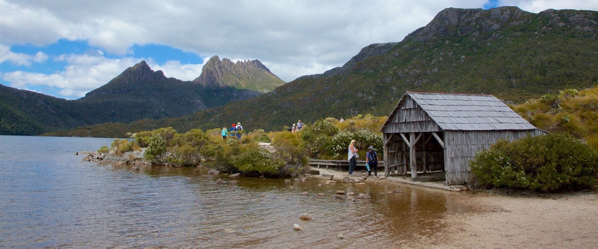 A lake with a wooden structure on the shore, surrounded by mountains and greenery.