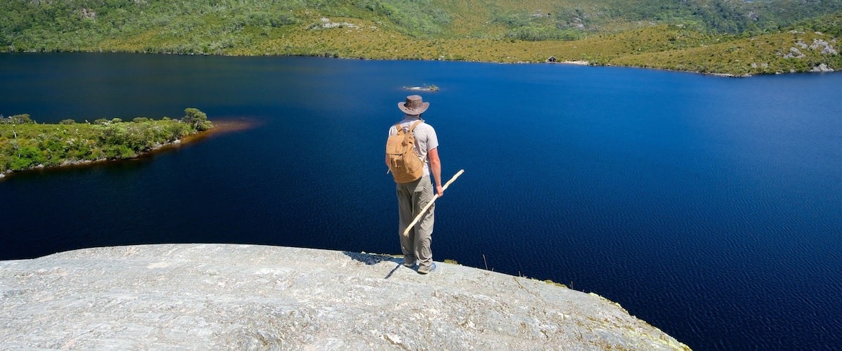 A person standing on a rocky outcrop overlooking a calm lake surrounded by green hills.