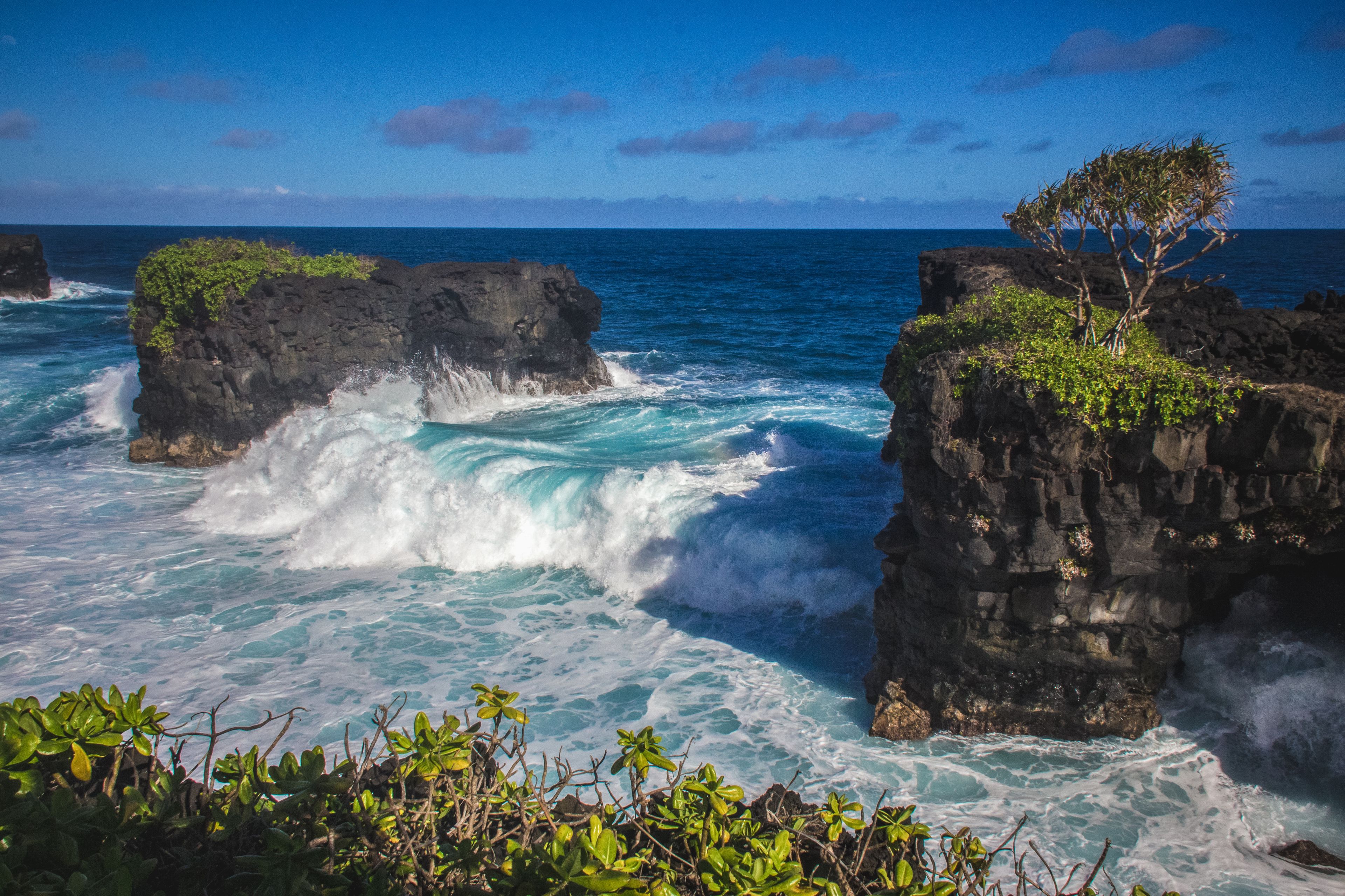 A rocky coastline with waves crashing against the rocks and a clear blue sky.