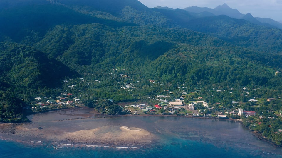A coastal town nestled between lush green hills and a clear blue sea.