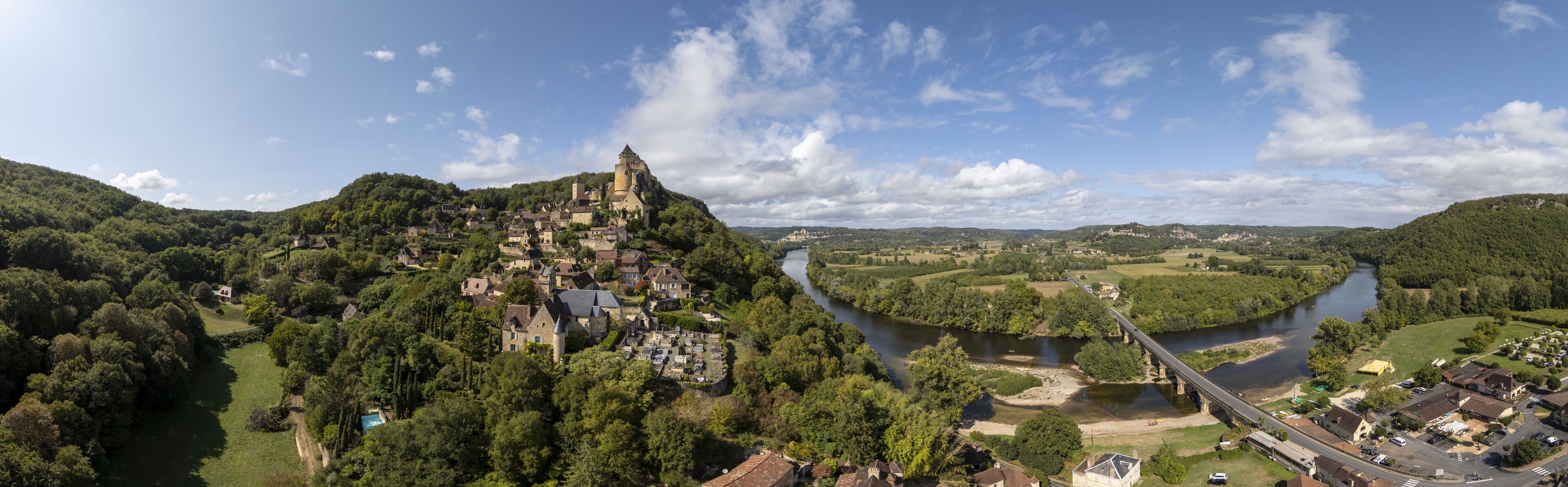 A panoramic view of a historic town with a castle on a hill, a river, and a bridge.