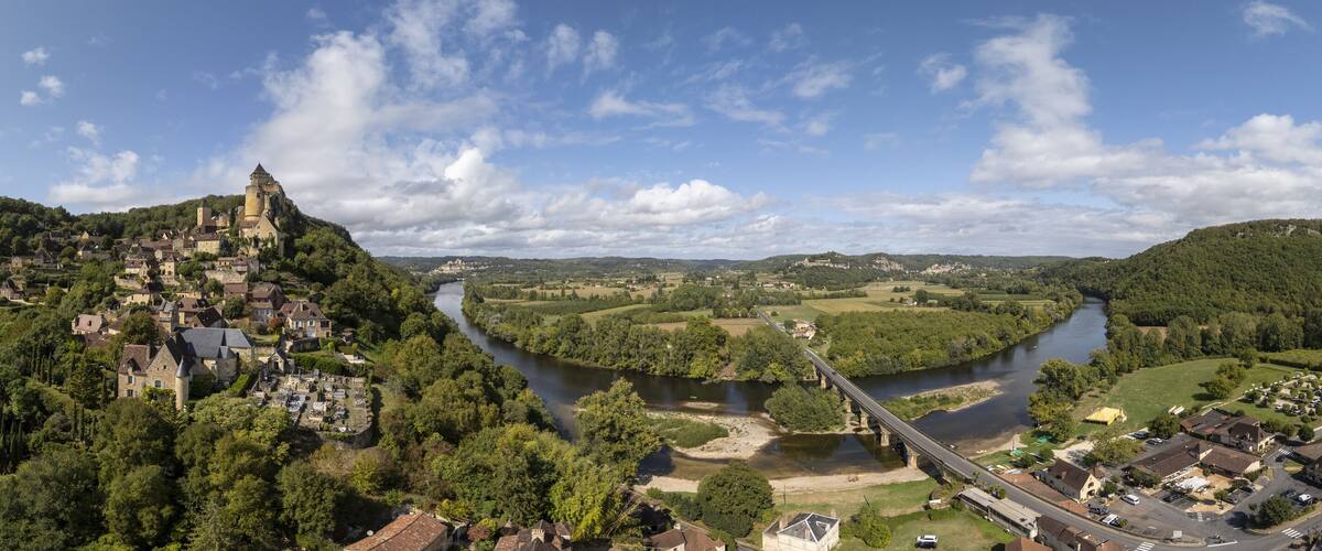 A panoramic view of a historic town with a castle on a hill, a river, and a bridge.