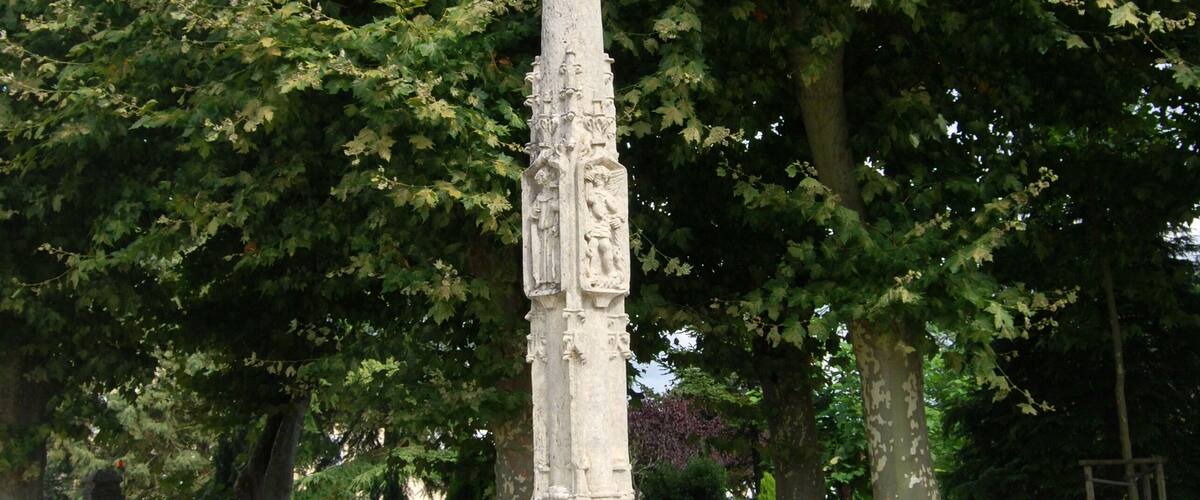A stone monument with carvings, surrounded by grass and trees.
