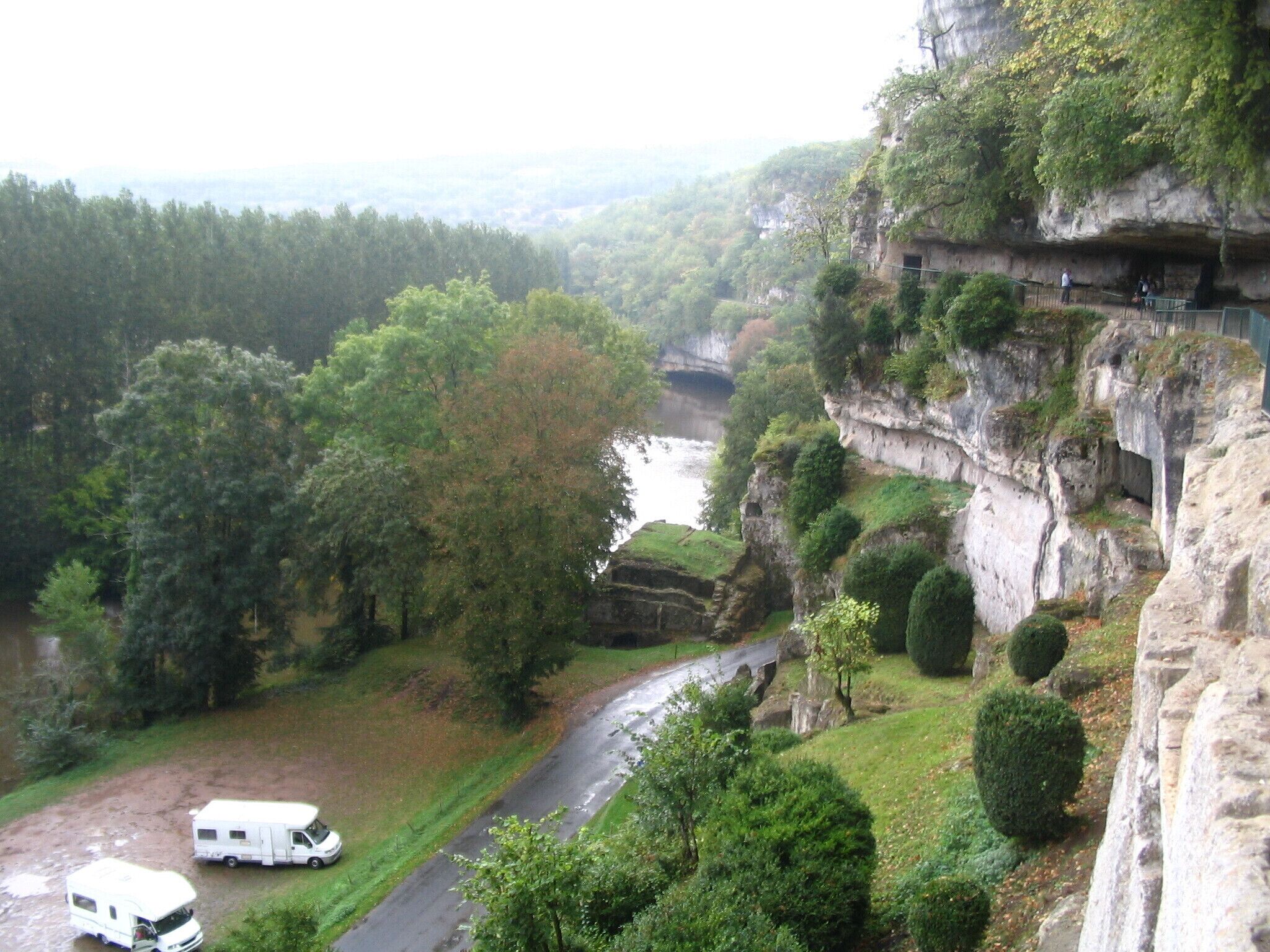 A river winding through a forested valley with a rocky cliff and a white camper parked on the side.