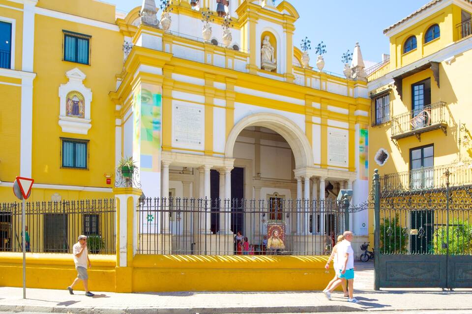 Un edificio amarillo con un arco blanco y columnas, rodeado por una cerca de hierro forjado.