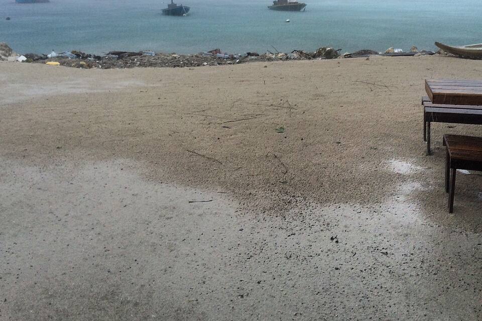 A beach with boats in the water and a rocky shoreline.