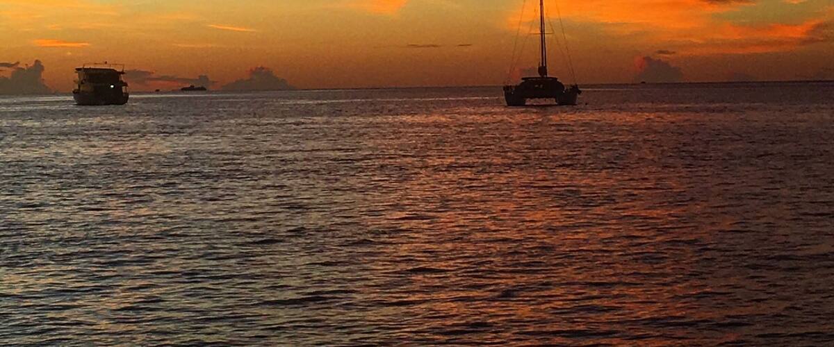 Un atardecer sobre un mar tranquilo con un velero y un barco a lo lejos.