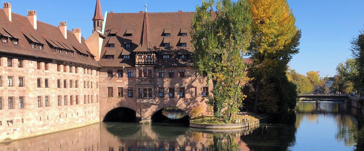 A historic building with a bridge over a calm river, surrounded by autumn foliage.